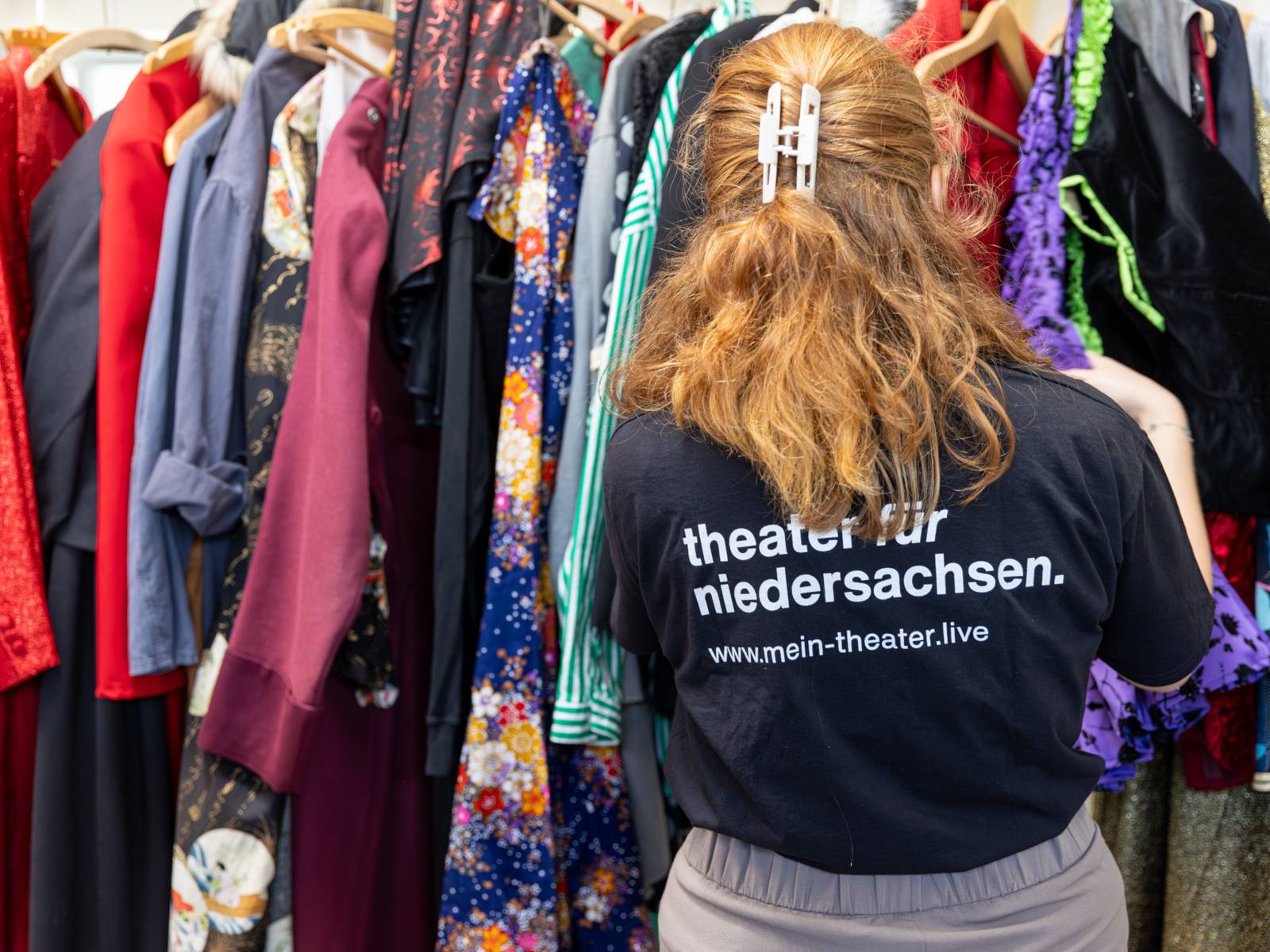 Eine Person vom Theater für Niedersachsen geht Kostüme durch, die auf Bügel gehängt sind.