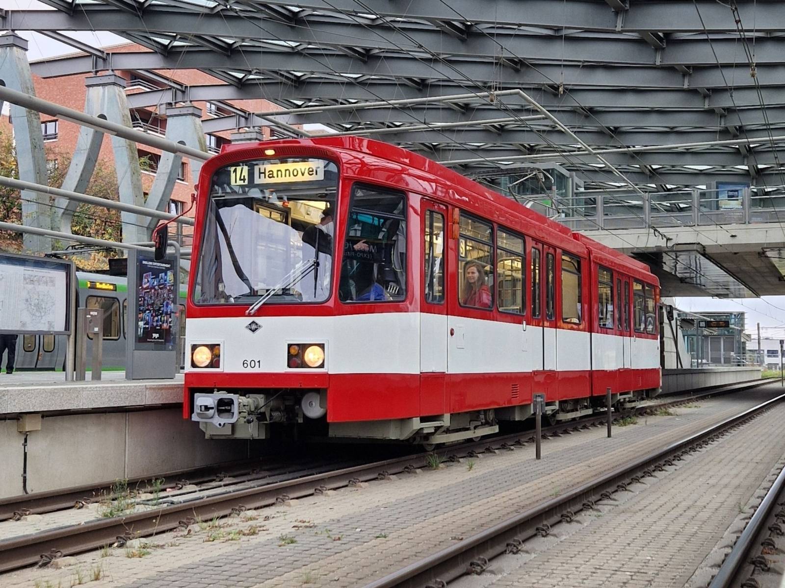 Eine rot und weiße Straßenbahn steht in einer Haltestelle auf den Schienen.
