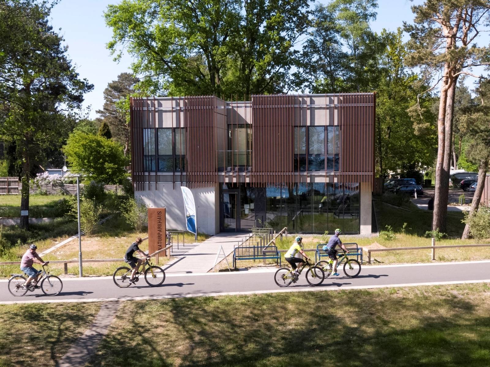 Vier Radfahrer fahren am Naturpark-Haus in Mardof vorbei.