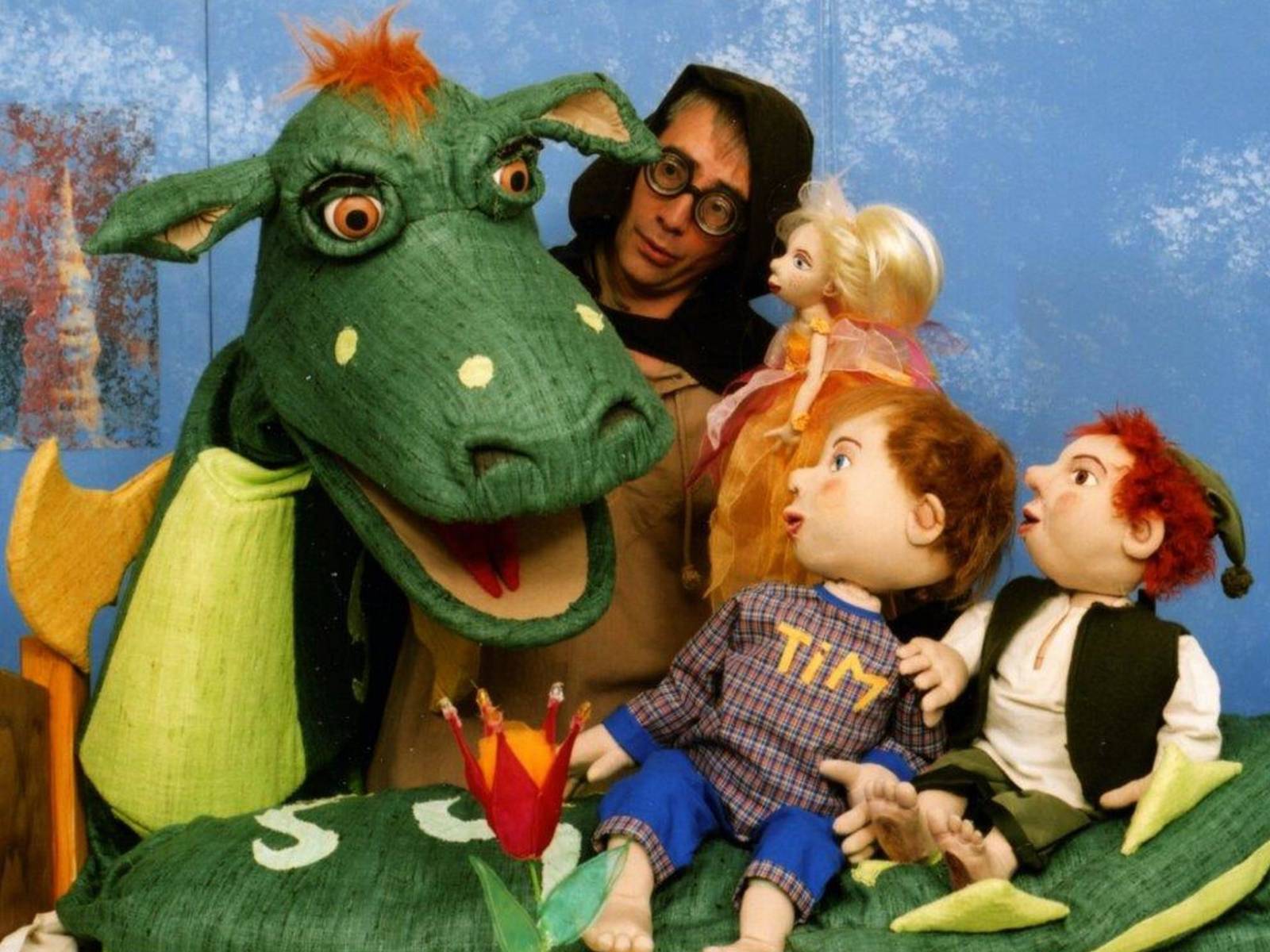 Ein Puppenspieler mit verschieden großen Puppen vor sich. Eine der Handpuppen ist ein großer Drache.