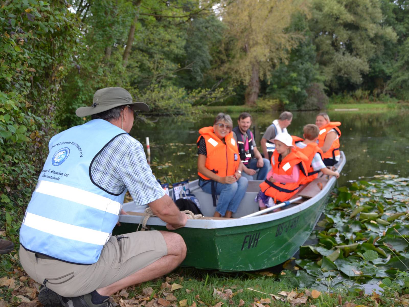 Ein kleines Boot mit Personen drin wird in hiesigem Gewässer zu Wasser gelassen
