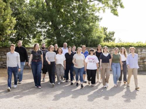 18 Personen gehen auf die Betrachter*in zu.