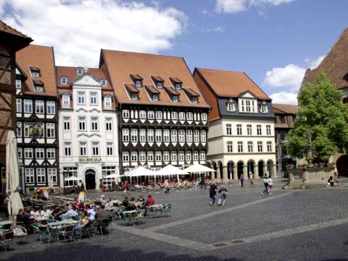 Mehrere historische, ganz unterschiedliche Häuser bilden eine Reihe. Die Häuser sind unterschiedlich hoch, zwei sind Fachwerkhäuser, eines hat einen Säulengang in der untersten Etage. Vor dieser Hausreihe bildet Kopfsteinpflaster den Marktplatz. Menschen sitzen auf Stühlen vor Cafés.