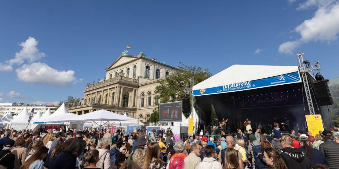 Menschen vor einer Bühne, im Hintergrund ist das Opernhaus Hannover zu sehen.