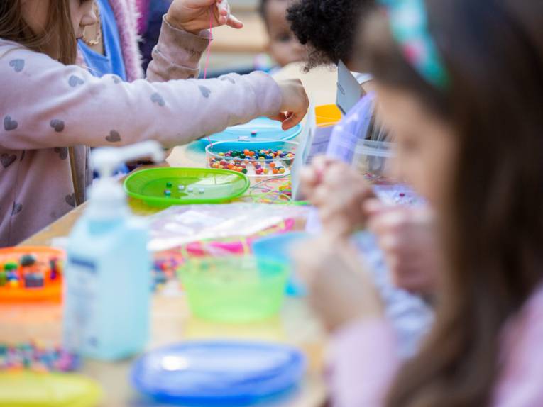 Kinder basteln an einem Tisch mit bunten Tellern und bunten Perlen