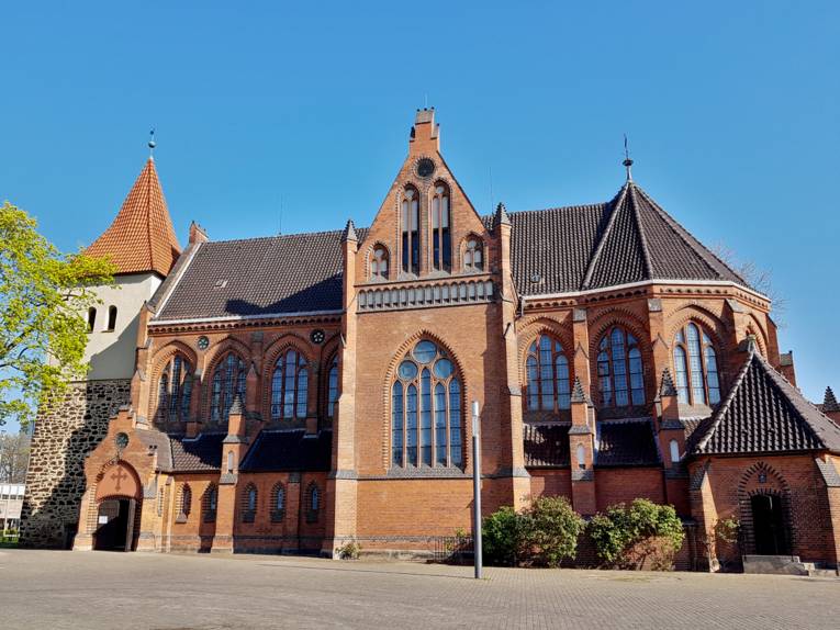 Neugotisches Kirchengebäude mit einem Kirchturm mit rotem Ziegeldach.