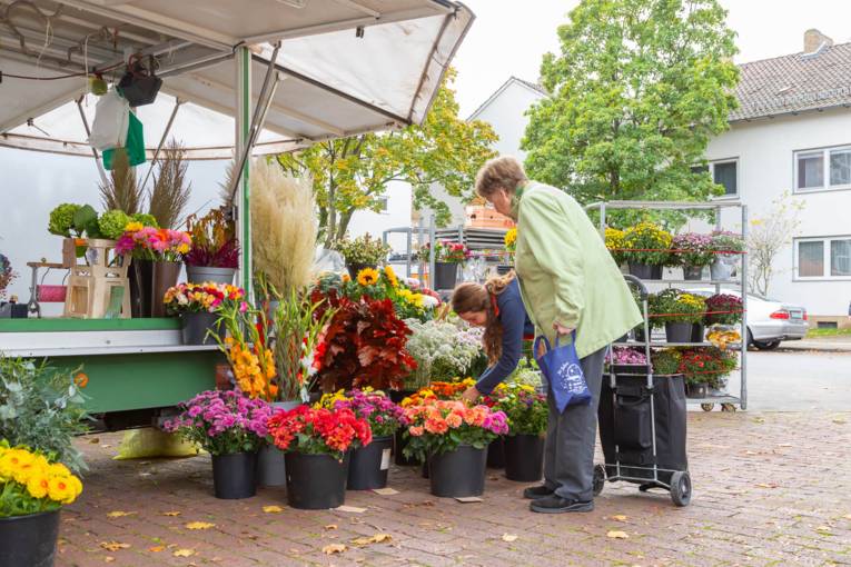 Eine Wochenmarkthändlerin berät eine Kundin zu ihrem Angebot.