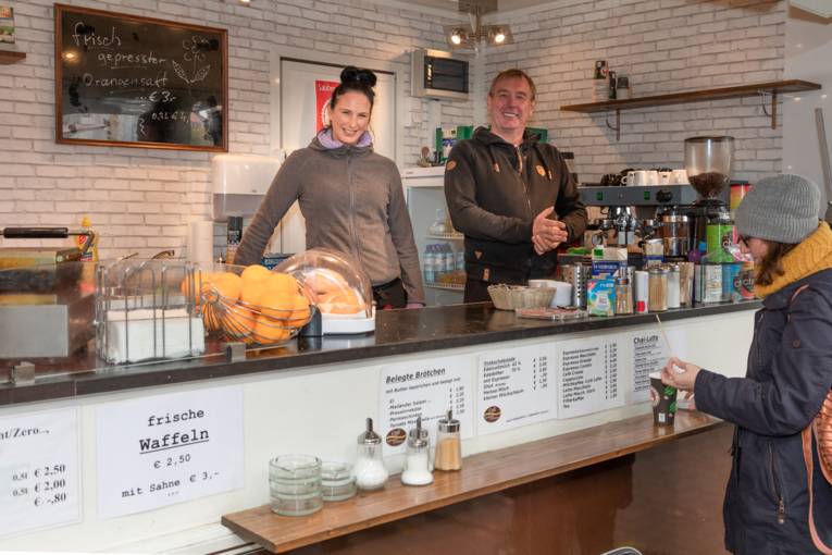 Verkaufspersonal und Kunden an einem Verkaufswagen für Kaffeespezialitäten und Snacks.