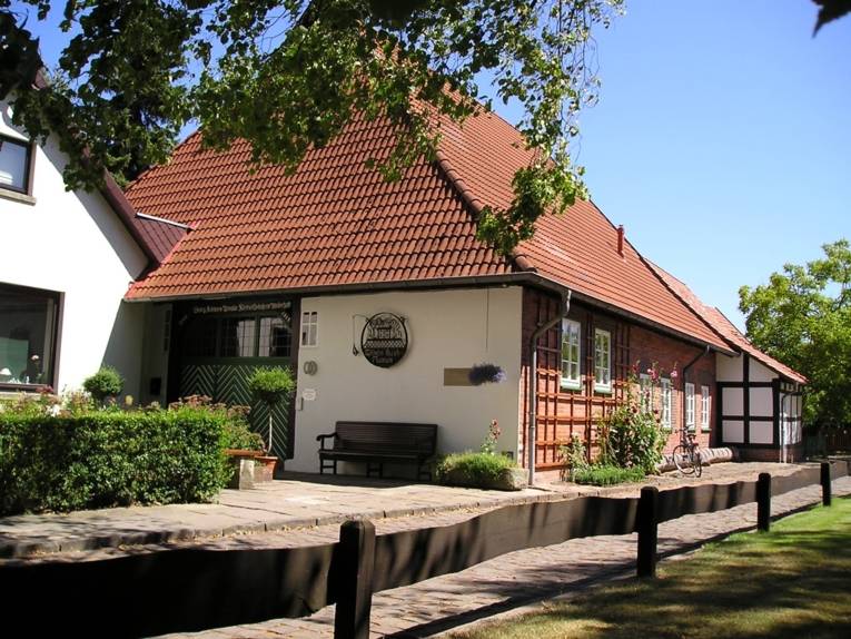 Hinter einem hölzernen Zaun steht  ein altes Backsteinhaus mit grüner Tür.