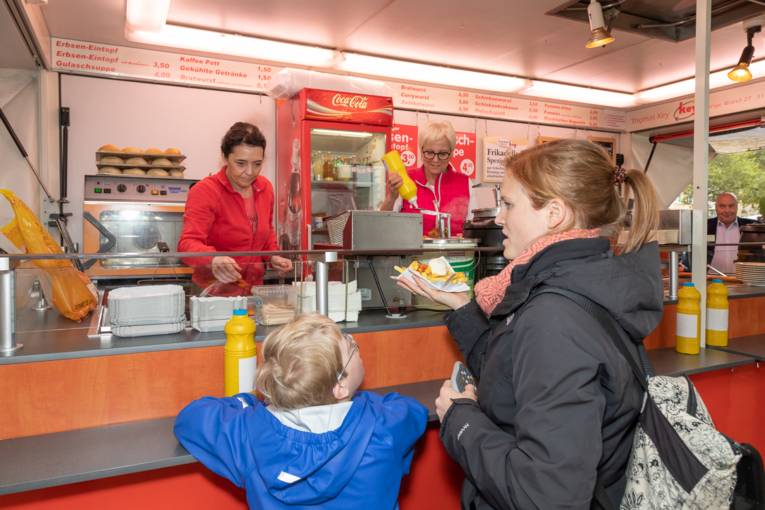 Eine Mutter und ihr Kind stehen an einer Imbissbude auf dem Wochenmarkt Stephansplatz