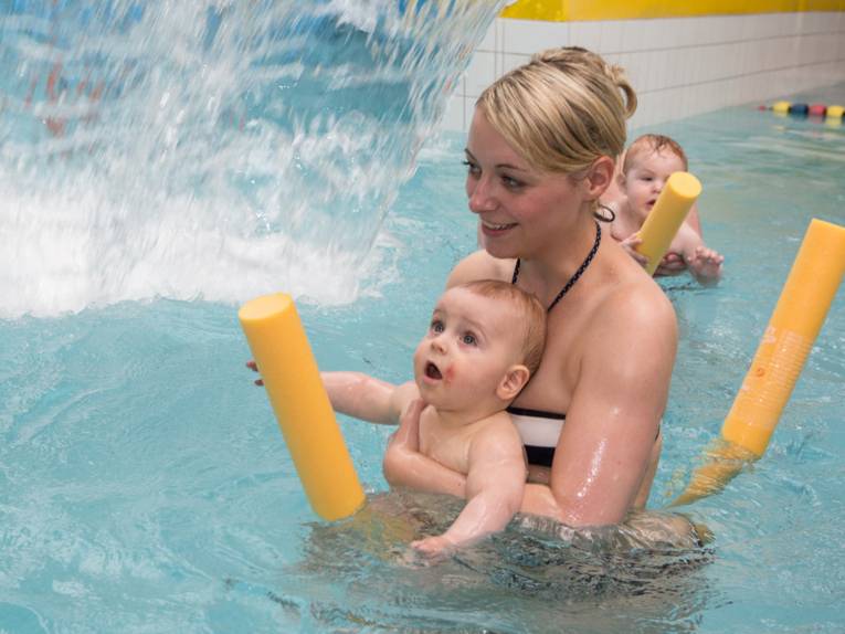 Mutter mit Baby im Hallenbad im Kinderbecken auf einer Poolnoodle