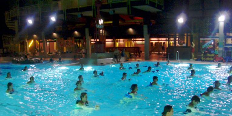 Badegäste haben sich im Schwimmbecken verteilt und folgen den Anweisungen des Trainers, der hier aber nicht im Bild zu sehen ist.