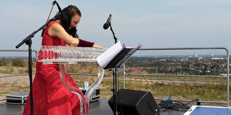 Eine Frau gibt ein Glasharfenkonzert und bringt verschiedene Trinkgläser mit unterschiedlichen Füllständen zum Schwingen.