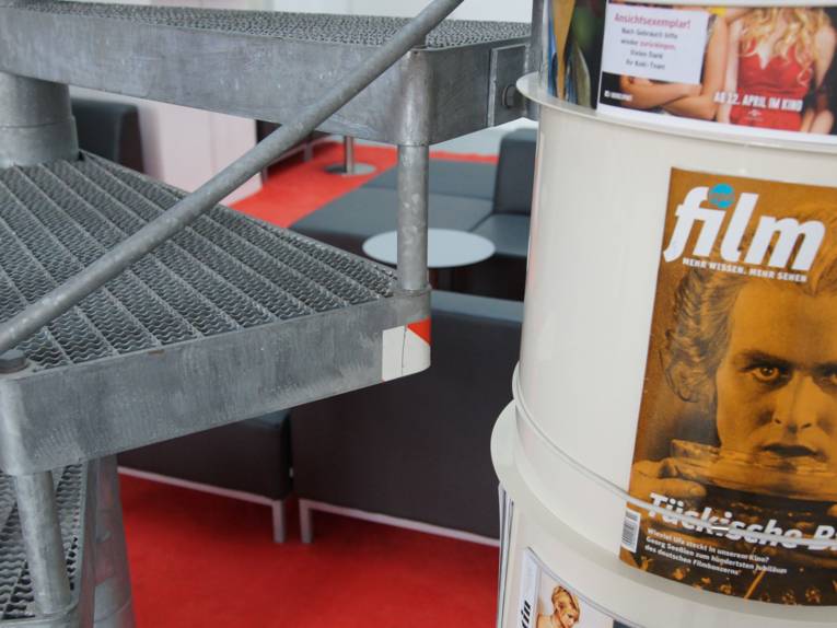 Ein Teil einer Wendeltreppe, dahinter befinden sich Sofas. 