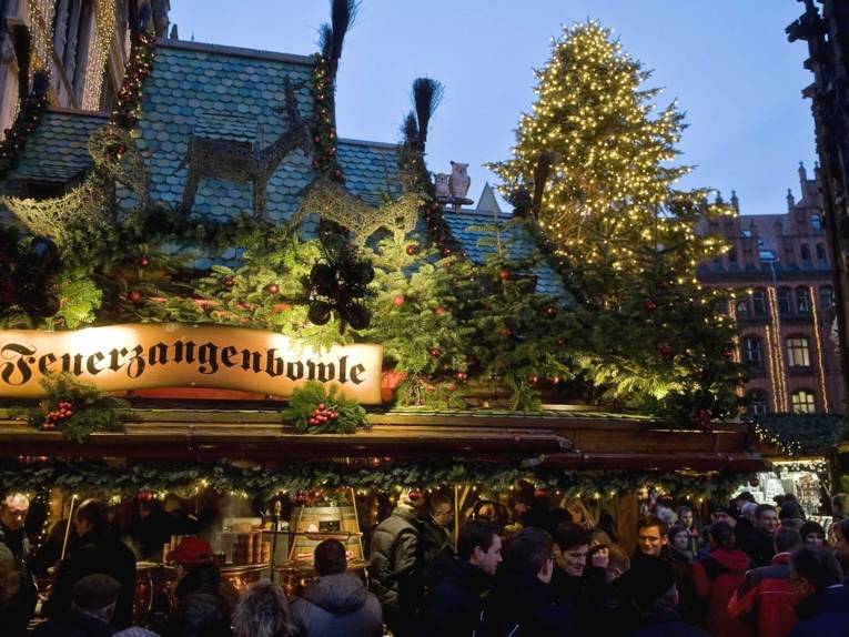 Ein weihnachtlich geschmückter Stand mit der beleuchteten Aufschrift "Feuerzangenbowle" auf dem Marktplatz neben der Marktkirche