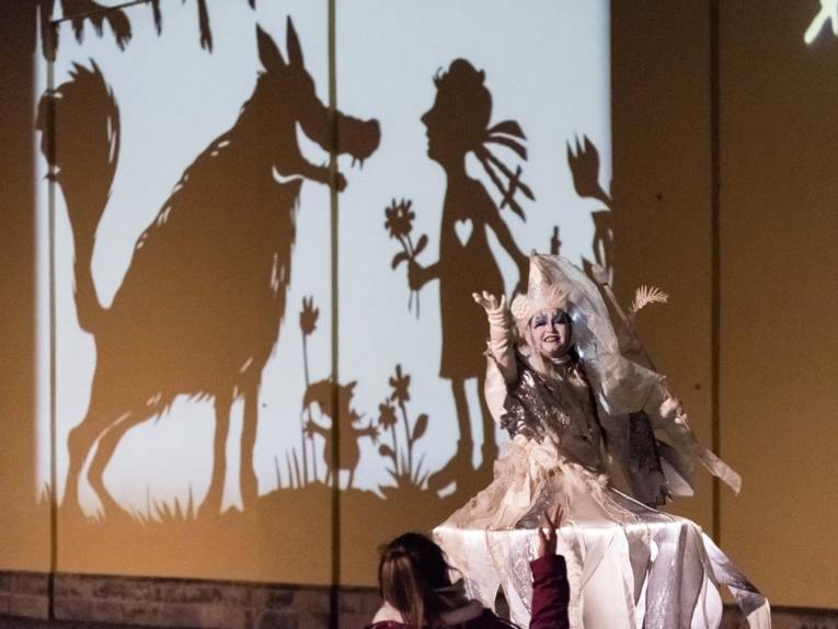 Illuminiertes Gebäude, davor eine Frau im weißen Kostüm. 