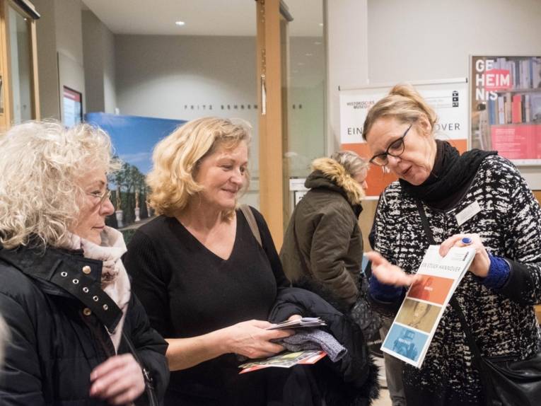 Zwei Frauen, die von einer anderen Frau Informationen zu einer Ausstellung bekommen. 