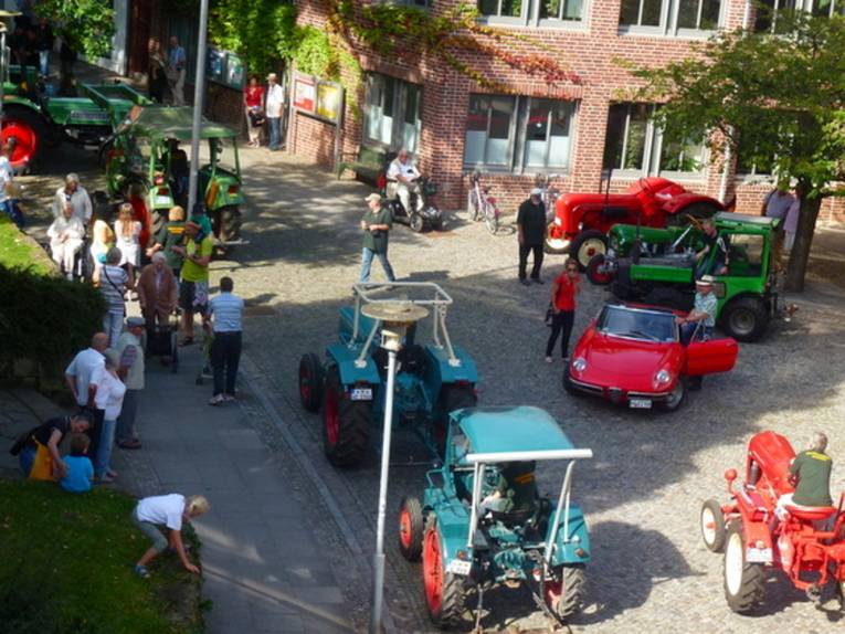 Aufnahme aus der Vogelperspektive: Sieben alte Traktoren und ein roter Sportwagen fahren durch Gehrden, Menschen stehen am Straßenrand und beobachten das bunte Treiben.