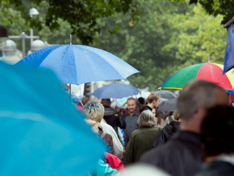 Viele Menschen gehen in Hannover auf dem Fußweg parallel zur Georgstraße, die meisten halten sich einen Regenschirm über den Kopf.