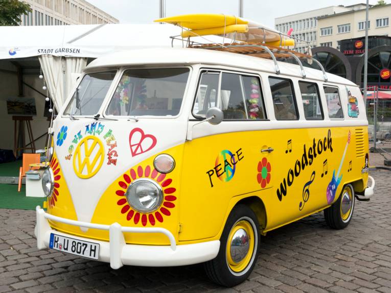 Ein VW Transporter t1 ist im Stil der Hippie-Bewegung lackiert und beschriftet. Blumen, das Friedenszeichen und weitere Symbole und Worte zieren den Lack.