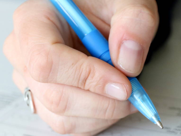 Eine Hand hält einen blauen Kugelschreiber und bewegt sich über ein Formular. Eine Hand hält einen blauen Kugelschreiber und bewegt sich über ein Formular.