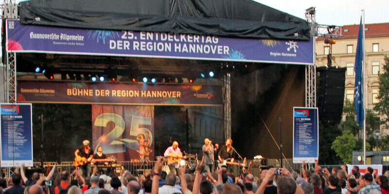 Die Bühne der Region Hannover ist die Hauptbühne beim Entdeckertag, sie steht in der Innenstadt von Hannover auf dem Opernplatz. Auf der Bühne spielen wingenfelder:Wingenfelder, davor drängt sich das Publikum. Die Menschen feiern ausgelassen, einige strecken ihre Arme nach oben und klatschen im Takt der Musik. Die Bühne der Region Hannover ist die Hauptbühne beim Entdeckertag, sie steht in der Innenstadt von Hannover auf dem Opernplatz. Auf der Bühne spielen wingenfelder:Wingenfelder, davor drängt sich das Publikum. Die Menschen feiern ausgelassen, einige strecken ihre Arme nach oben und klatschen im Takt der Musik.