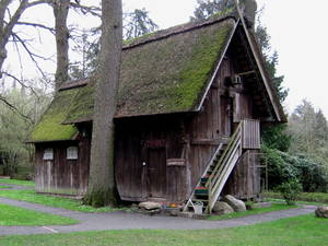 Altes Holzhaus mit spitzem Giebel. Das Dach ist mit Reet oder Stroh eingedeckt und zum großem Teil mit grünem Moos bedeckt. Eine Außentreppe aus Holz führt auf den Dachboden. Altes Holzhaus mit spitzem Giebel. Das Dach ist mit Reet oder Stroh eingedeckt und zum großem Teil mit grünem Moos bedeckt. Eine Außentreppe aus Holz führt auf den Dachboden.