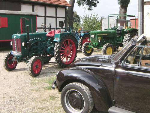 Im Hintergrund stehen drei Oldtimertraktoren, zum Beispiel ein Hanomag. Davor steht ein Käfer-Cabriolet. Im Hintergrund stehen drei Oldtimertraktoren, zum Beispiel ein Hanomag. Davor steht ein Käfer-Cabriolet.