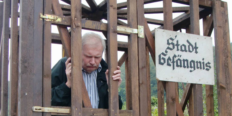 Ein Mann ist in einen Holzverschlag gesperrt, auf einem Schild steht "Stadt Gefängnis". Ein Mann ist in einen Holzverschlag gesperrt, auf einem Schild steht "Stadt Gefängnis".