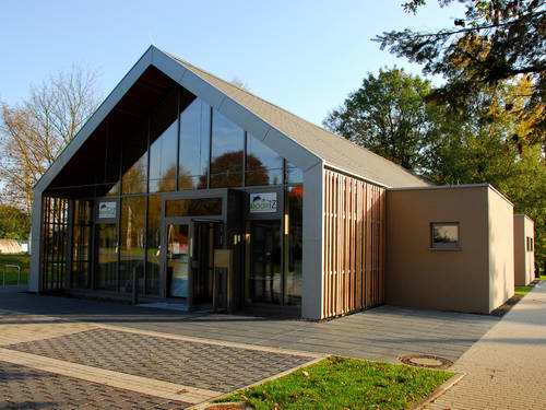 Modernes, eingeschossiges Gebäude mit Spitzdach und zwei würfelförmigen Anbauten. Vor dem Gebäude befinden sich Parkplätze und Fahrradbügel. Modernes, eingeschossiges Gebäude mit Spitzdach und zwei würfelförmigen Anbauten. Vor dem Gebäude befinden sich Parkplätze und Fahrradbügel.