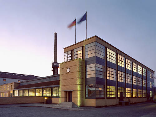Beleuchtetes Fagus-Werk vor blaume Himmel. Auf dem Dach wehen die Fahne der Europäischen Union und die Fahne der Bundesrepublik Deutschland im Wind. Beleuchtetes Fagus-Werk vor blaume Himmel. Auf dem Dach wehen die Fahne der Europäischen Union und die Fahne der Bundesrepublik Deutschland im Wind.