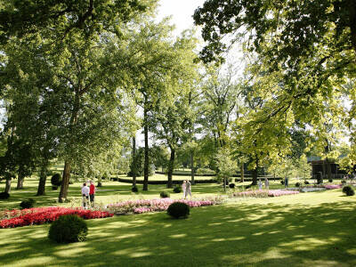 Rasenfläche, Blumenbeete und Wege mit spazierenden Menschen, drum herum stehen hohe Laubbäume. Rasenfläche, Blumenbeete und Wege mit spazierenden Menschen, drum herum stehen hohe Laubbäume.
