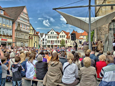 Menschen verfolgen ein Schauspiel, Fachwerkhäuser stehen um den Platz. Menschen verfolgen ein Schauspiel, Fachwerkhäuser stehen um den Platz.