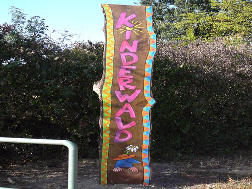 Auf einem Holzschild steht der Schriftzug "KINDERWALD". Auf einem Holzschild steht der Schriftzug "KINDERWALD".