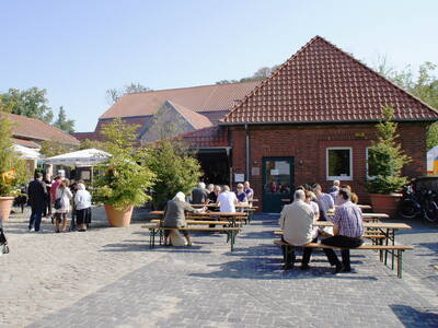 Gepflasterter Hof, im Hintergrund Gebäude aus roten Backsteinen. Menschen sitzen auf Festzeltgarnituren. Gepflasterter Hof, im Hintergrund Gebäude aus roten Backsteinen. Menschen sitzen auf Festzeltgarnituren.