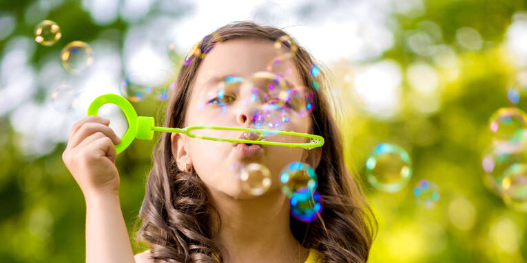 Ein Mädchen trägt ein gelbes Sommerkleid und macht Seifenblasen. Der Hintergrund ist grün. Ein Mädchen trägt ein gelbes Sommerkleid und macht Seifenblasen. Der Hintergrund ist grün.