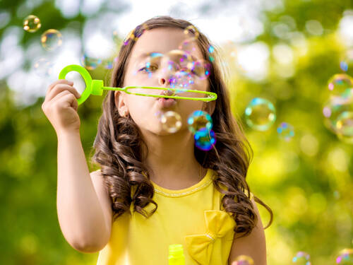 Ein Mädchen trägt ein gelbes Sommerkleid und macht Seifenblasen. Der Hintergrund ist grün. Ein Mädchen trägt ein gelbes Sommerkleid und macht Seifenblasen. Der Hintergrund ist grün.