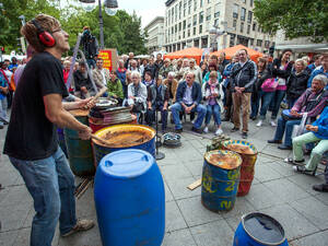 Ein Musiker trommelt auf einer blauen Tonne aus Plastik, vor und neben ihm stehen weitere Fässer, diese sind aber zum größten Teil aus Metall. Ein Musiker trommelt auf einer blauen Tonne aus Plastik, vor und neben ihm stehen weitere Fässer, diese sind aber zum größten Teil aus Metall.