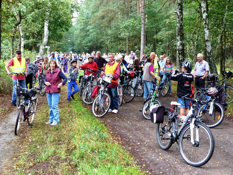 Fahrradfahrer haben ihrer Räder auf und neben einem Waldweg abgestellt, die meisten Leute stehen bei ihrem Rad und blicken in Richtung der Kamera. Fahrradfahrer haben ihrer Räder auf und neben einem Waldweg abgestellt, die meisten Leute stehen bei ihrem Rad und blicken in Richtung der Kamera.