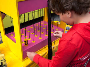 Ein Mädchen sitzt vor einem Spielgerät, an dem Fäden gezogen werden. Ein Mädchen sitzt vor einem Spielgerät, an dem Fäden gezogen werden.