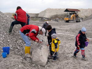 Erwachsene und Kinder arbeiten sich mit dem Hammer durch Kalkgestein. Sie tragen dabei Gummistiefel und Regenjacken. Fundstücke werden in Plastikeimern verstaut. Erwachsene und Kinder arbeiten sich mit dem Hammer durch Kalkgestein. Sie tragen dabei Gummistiefel und Regenjacken. Fundstücke werden in Plastikeimern verstaut.