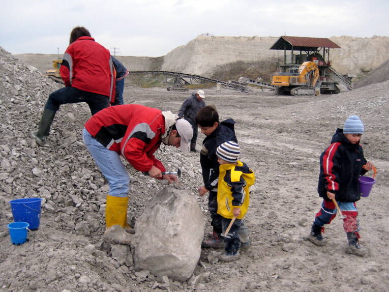 Erwachsene und Kinder arbeiten sich mit dem Hammer durch Kalkgestein. Sie tragen dabei Gummistiefel und Regenjacken. Fundstücke werden in Plastikeimern verstaut. Erwachsene und Kinder arbeiten sich mit dem Hammer durch Kalkgestein. Sie tragen dabei Gummistiefel und Regenjacken. Fundstücke werden in Plastikeimern verstaut.