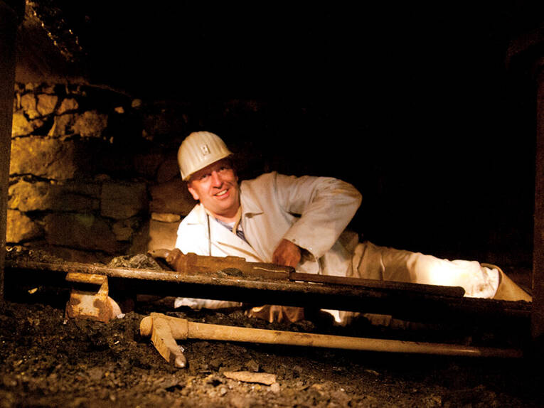 Ein Bergmann liegt in einem niedrigen Stollen, vor ihm liegt eine Spitzhacke. Ein Bergmann liegt in einem niedrigen Stollen, vor ihm liegt eine Spitzhacke.